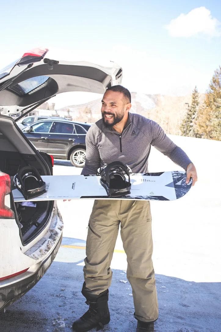 BTB Jordan Layao Image 1 A smiling man in winter gear holds a snowboard beside an open car trunk against a snowy mountain backdrop.
