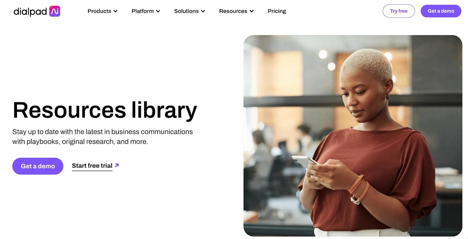 dialpad resources A woman with short hair in a brown shirt looks at her phone in a modern office setting.
