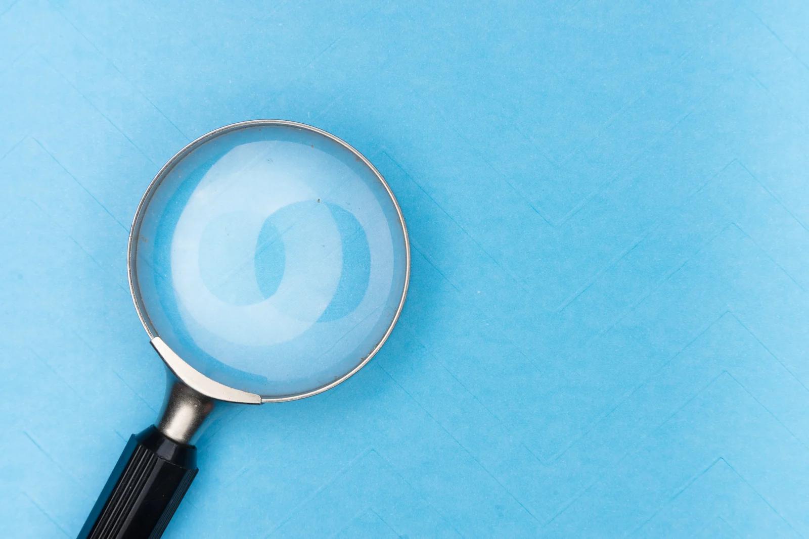 A black magnifying glass laying on a baby blue surface.
