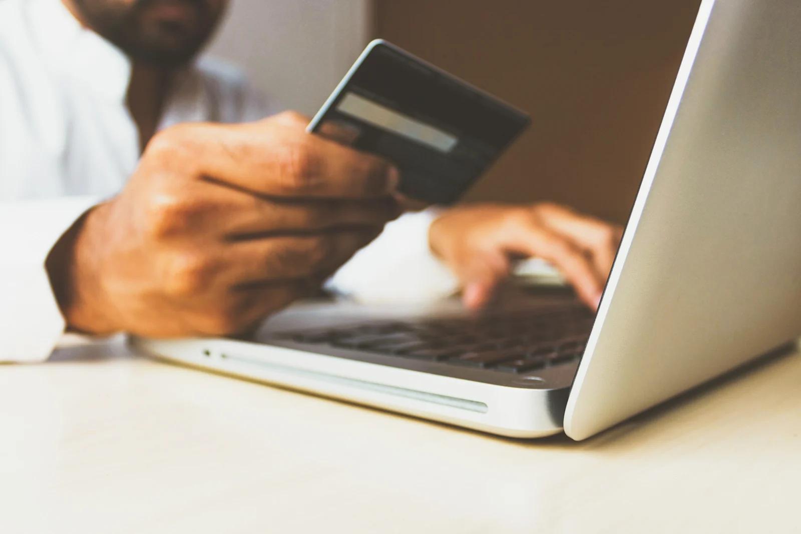 An image of a person on a computer while holding his credit card in his hand.