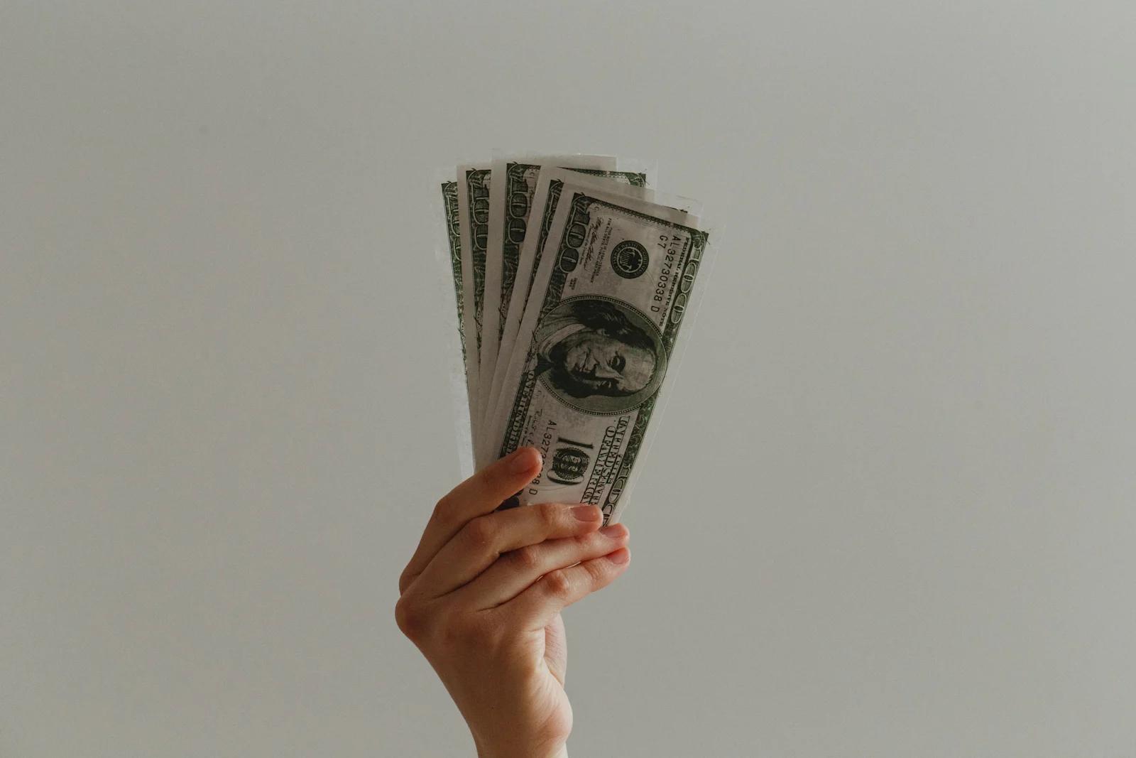 An image of a hand holding five one hundred dollar bills.