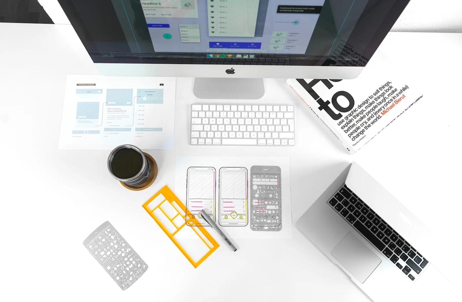 Image of an Apple Mac desktop with UX design materials laying on a white table.